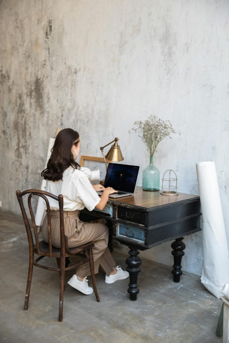 Woman working on a laptop in a vintage styled home office setup.